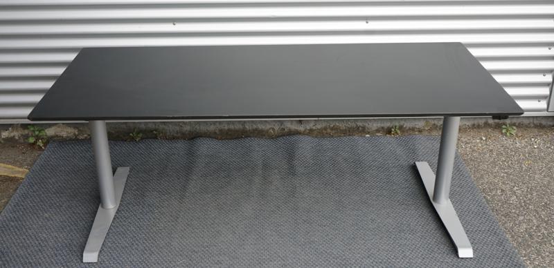 Frontbillede af Omann hæve-sænkebord 180x90 med sort bordplade, affasede kanter, gråt understel og kabelbakke.